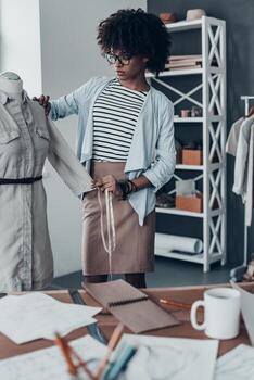 todo debe ser perfecto. hermosa joven africana midiendo la manga con cinta mientras está de pie en su taller foto