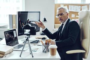 Senior man in elegant business suit using modern technologies while making social media video photo
