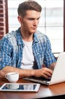 aprovechando las ventajas del wi-fi gratuito. un joven apuesto que trabaja en una laptop mientras está sentado en la mesa foto
