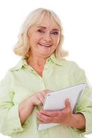 Taking advantages of digital age. Cheerful senior woman using digital tablet and smiling while standing isolated on white background photo