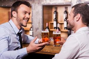 Friday night fun. Two cheerful young men in shirt and tie talking to each other and gesturing while drinking beer at the bar counter photo