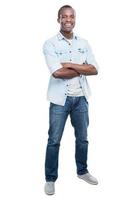 Casually handsome. Full length of handsome young black man keeping arms crossed and smiling at camera while standing against white background photo