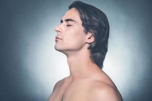 Fresh and clean. Side view of young shirtless man keeping eyes closed and looking calm while standing against grey background photo