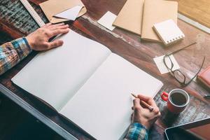 Start planning today. Close-up top view image of man writing in notebook with copy space while sitting at the rustic wooden table photo