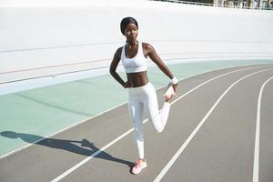 Full length of confident young African woman in sports clothing doing stretching exercises outdoors photo
