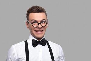 I know a lot of things. Portrait of young nerd man in bow tie and suspenders looking at camera and smiling while standing against grey background photo