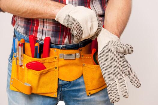 Getting ready to work. Close-up of handyman with tool belt wearing protective gloves while standing  against grey background photo