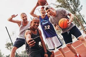 volviendo locos juntos. grupo de hombres jóvenes en ropa deportiva tomando selfie y sonriendo mientras están de pie al aire libre foto