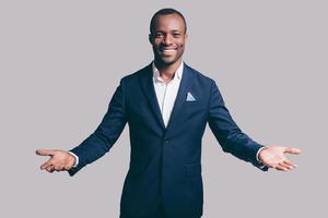 You are welcome Handsome young African man in smart casual jacket gesturing and smiling while standing against grey background photo