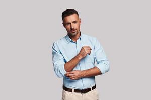 Ready to do things. Handsome young man adjusting sleeve and looking at camera while standing against grey background photo