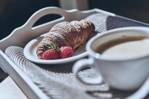 Great morning meal. Close up of croissant, strawberry and a cup of coffee on the tray photo