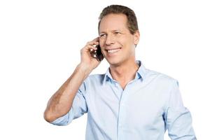 Good talk. Happy mature man talking on the mobile phone and smiling while standing against white background photo