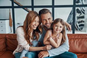 familia joven feliz sonriendo y mirando a la cámara mientras se unen en casa foto