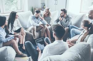 Everything will be alright. Group of young people sitting in circle while one man holding head in hand and looking upset while young woman comforting him photo