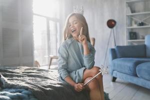 Cute little girl gesturing and smiling while playing with a magic wand at home photo