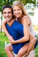 Having fun together. Low angle view of beautiful young loving couple standing outdoors together while woman hugging her boyfriend and smiling