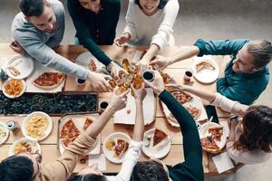 grupo de jóvenes con ropa informal recogiendo pizza y sonriendo mientras cenan en el interior foto