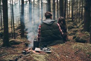 Real soul mates. Rear view of young couple warming up by the campfire while sitting in the forest photo