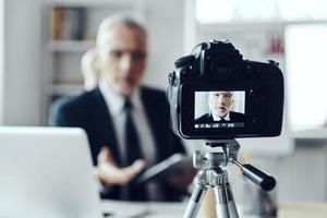 Senior man in elegant business suit using digital tablet while making social media video photo