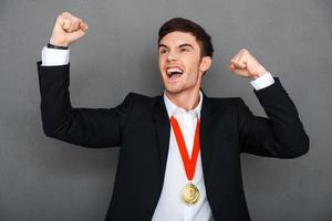 Always first. Happy young man in formalwear keeping arms raised and expressing positivity while standing against grey background photo