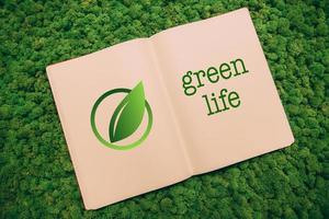 Green life. Top view close-up image of notebook with leaf symbol and text at moss background photo