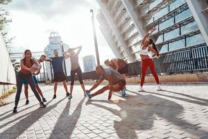 Longitud total de personas con ropa deportiva calentándose y estirándose mientras hacen ejercicio al aire libre foto