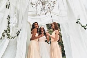 With her ladies by her side. Attractive young bride drinking champagne with her beautiful bridesmaids while standing outdoors photo