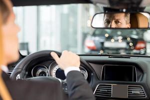 Feeling confident in his new car. Rear view of confident senior man in formalwear sitting on drivers place in car and looking at mirror photo