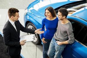 Buying their first car together. High angle view of young car salesman standing at the dealership telling about the features of the car to the customers photo