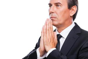 Praying for success. Side view of thoughtful mature man in formalwear holding hands clasped near face and looking away while standing isolated on white background photo