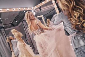 Big moment is coming.  Reflection of young woman adjusting a wedding dress on attractive bride while standing in the fitting room photo