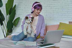 Teenage girl using laptop while sitting on bed with her dog photo