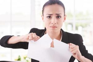 Breaking contract. Furious young woman in formalwear tearing up paper while sitting at the table photo