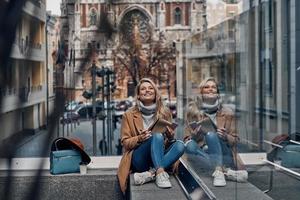 Attractive young woman listening music using her smart phone and smiling while spending carefree time in the city photo