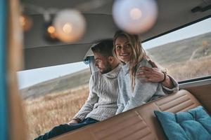 She is the center of his universe. Beautiful young couple resting and smiling while sitting in retro style mini van photo