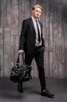 Stylish handsome. Full length of handsome young man in formalwear carrying a black bag photo