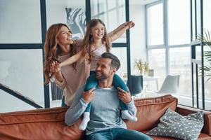 familia joven feliz sonriendo y abrazándose mientras se unen en casa foto