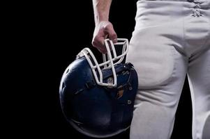 Crash helmet.  Cropped image of American football player holding football helmet while standing against black background photo