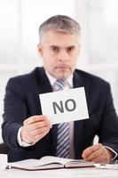 Rejected Confident senior man in formalwear holding a paper with no sign on it while sitting at her working place photo