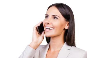 buena plática. confiada joven mujer de negocios en traje hablando por teléfono móvil y sonriendo mientras está aislada en el fondo blanco foto