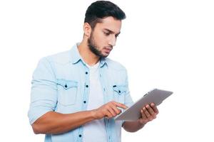 Man with digital tablet. Handsome young Indian man working on digital tablet while standing against white background photo