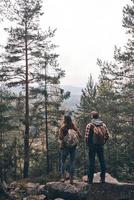 Full length rear view of young couple admiring the view while hiking together in the woods photo