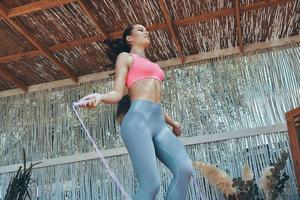 Low angle view of beautiful young woman in sports clothing using jumping rope on patio photo