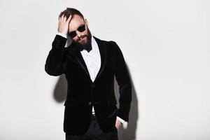 He got perfect style. Handsome young man in full suit keeping hand in hair while standing against grey background photo