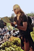 Where to go next Handsome young man in casual clothing looking at map while standing on the hill outdoors photo