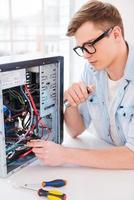 Trying to find what was broken.  Portrait of handsome young man repairing computer while sitting at his working place photo