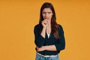 Thoughtful young woman in casual looking away while standing against yellow background photo