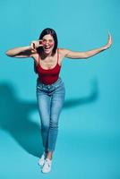 Full length of attractive young woman looking at camera and smiling while standing against blue background photo