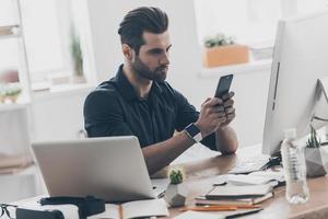 Texting am important message. Handsome young man typing a message with a serious face while sitting at the desk in creative office photo