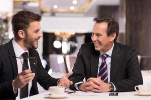 Great success. Two cheerful business people in formalwear discussing something and smiling while sitting at the restaurant photo